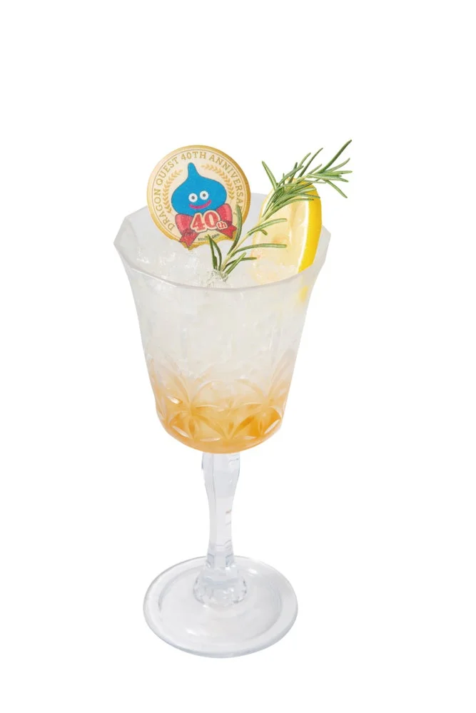 透明なグラスに入った冷たい飲み物で、レモンスライスとローズマリーが添えられています。ドラゴンクエスト40周年記念のスライムの飾りも付いています。