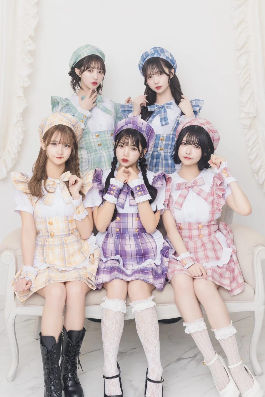 パステルカラーのチェック柄メイド服とベレー帽を着用した5人の若い女性が白いソファに座っているポートレート