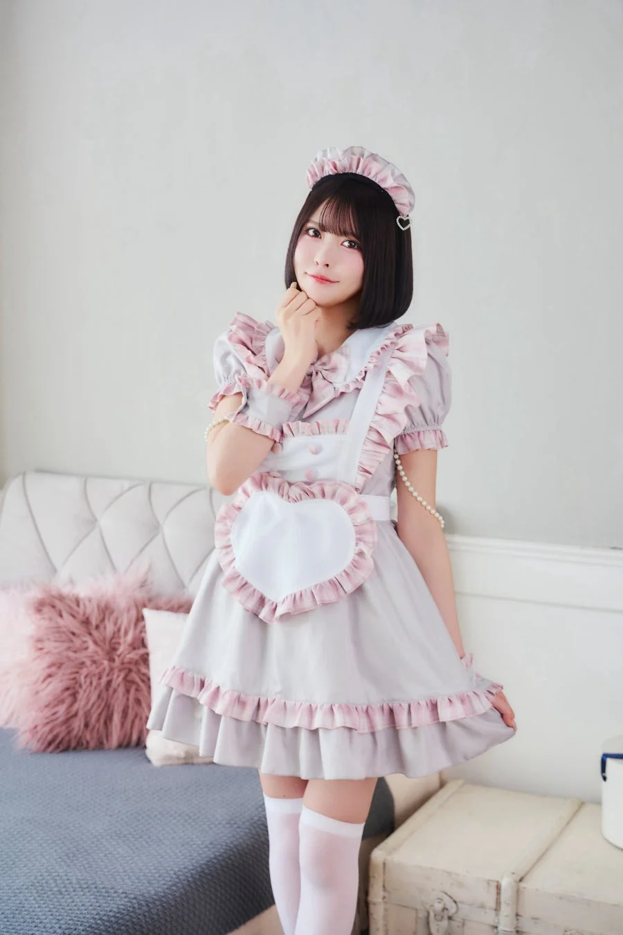 ピンクとグレーのフリル付きメイド服を着た若い女性が、可愛らしいポーズで立っているポートレート