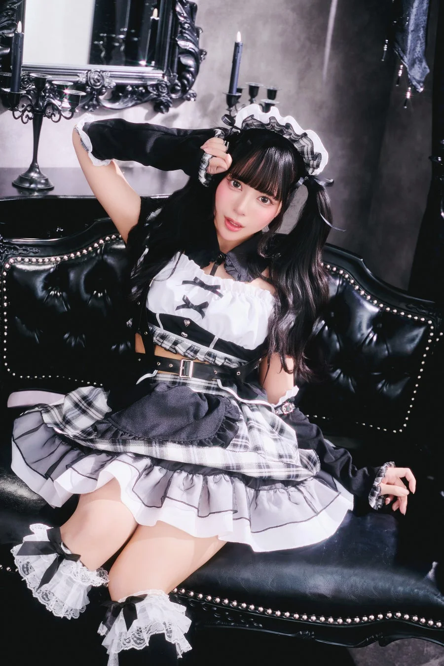 ゴシック調のメイド服を着用した女性が、黒い革張りのソファに座っています