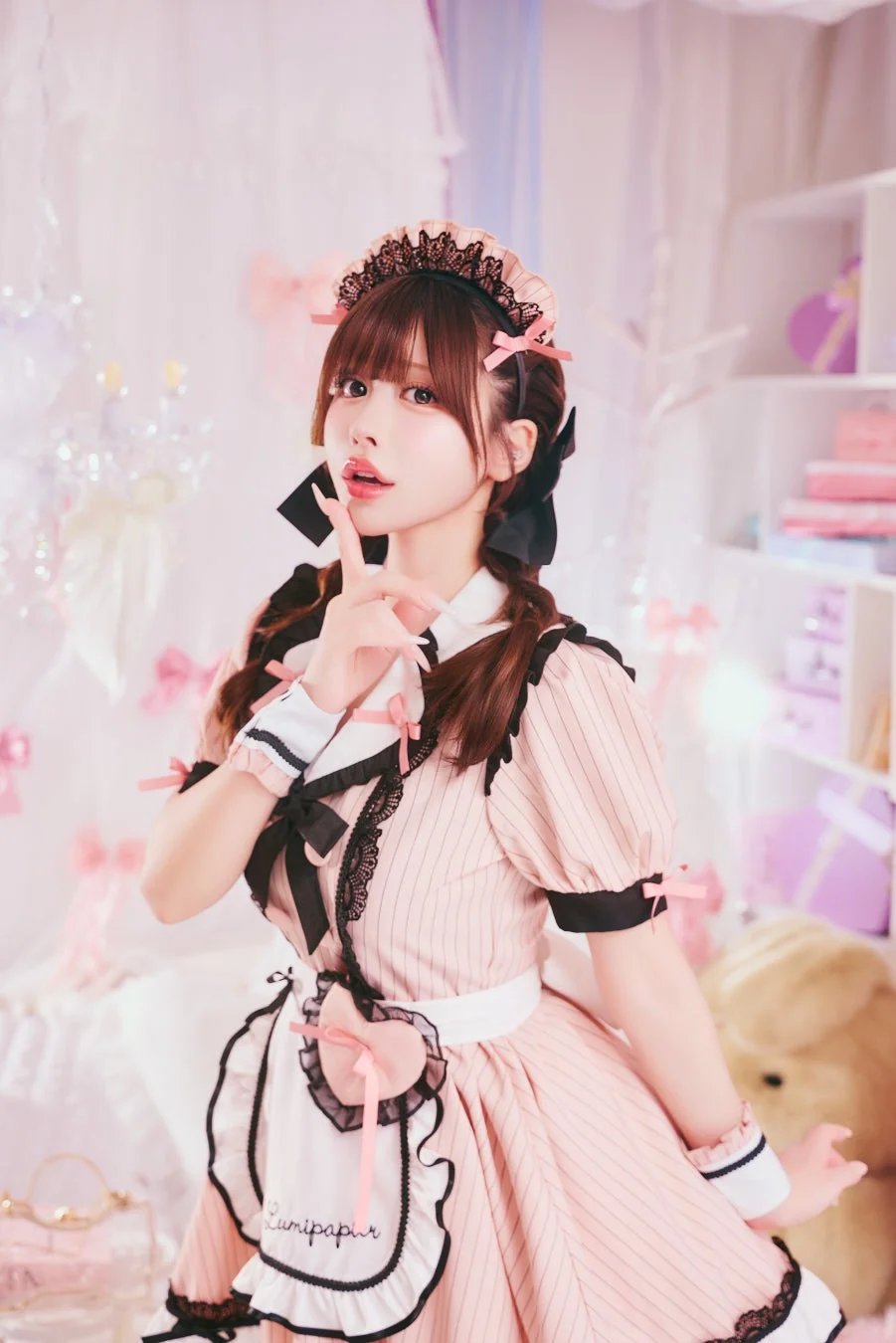 ピンクのストライプ柄のメイド服を着た女性が、指を口元に当ててポーズをとっています