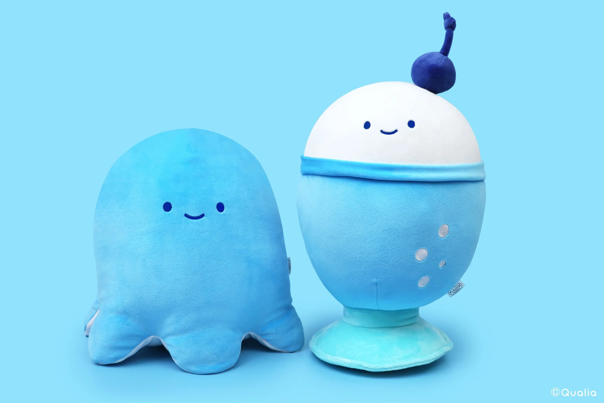 水色の背景に、タコとアイスクリームのような形をした二つの可愛らしい青いぬいぐるみが並んでいます。どちらもシンプルな笑顔の表情で、見る人に癒しを与えます。