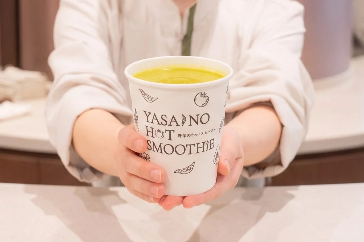 白い紙コップに入った緑色のホットスムージーを両手で持っている人物のクローズアップ