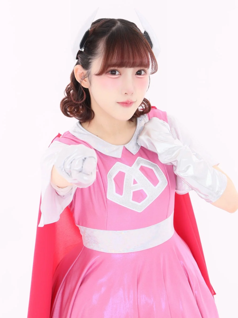 ピンク色のコスチュームと赤いケープを身につけた女性が拳を構える