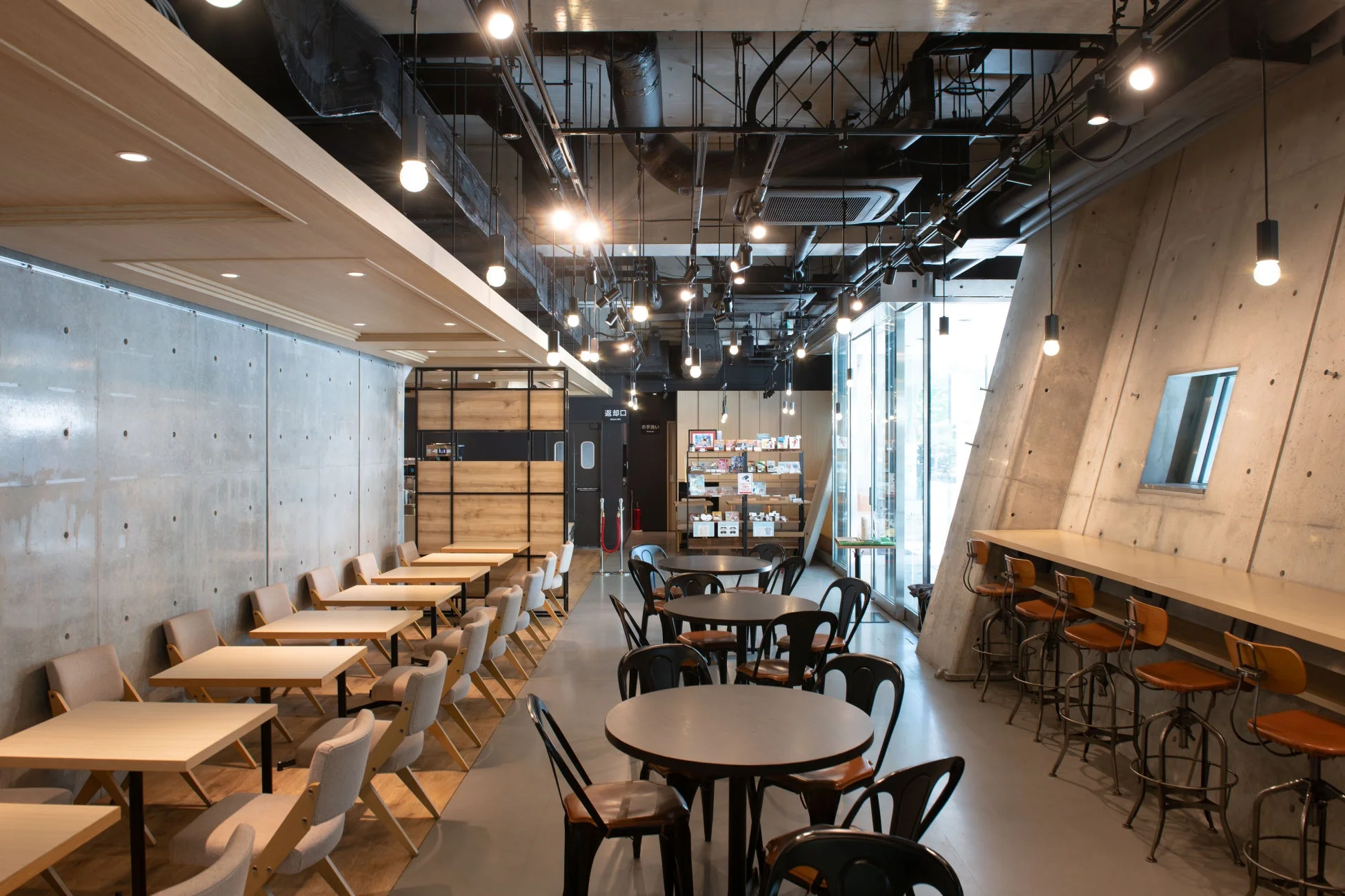 カフェ,ラウンジ,モダンインテリア,コンクリート壁,木材,おしゃれな空間,テーブル席,カウンター席,工業デザイン,休憩スペース,商業施設,デザインオフィス