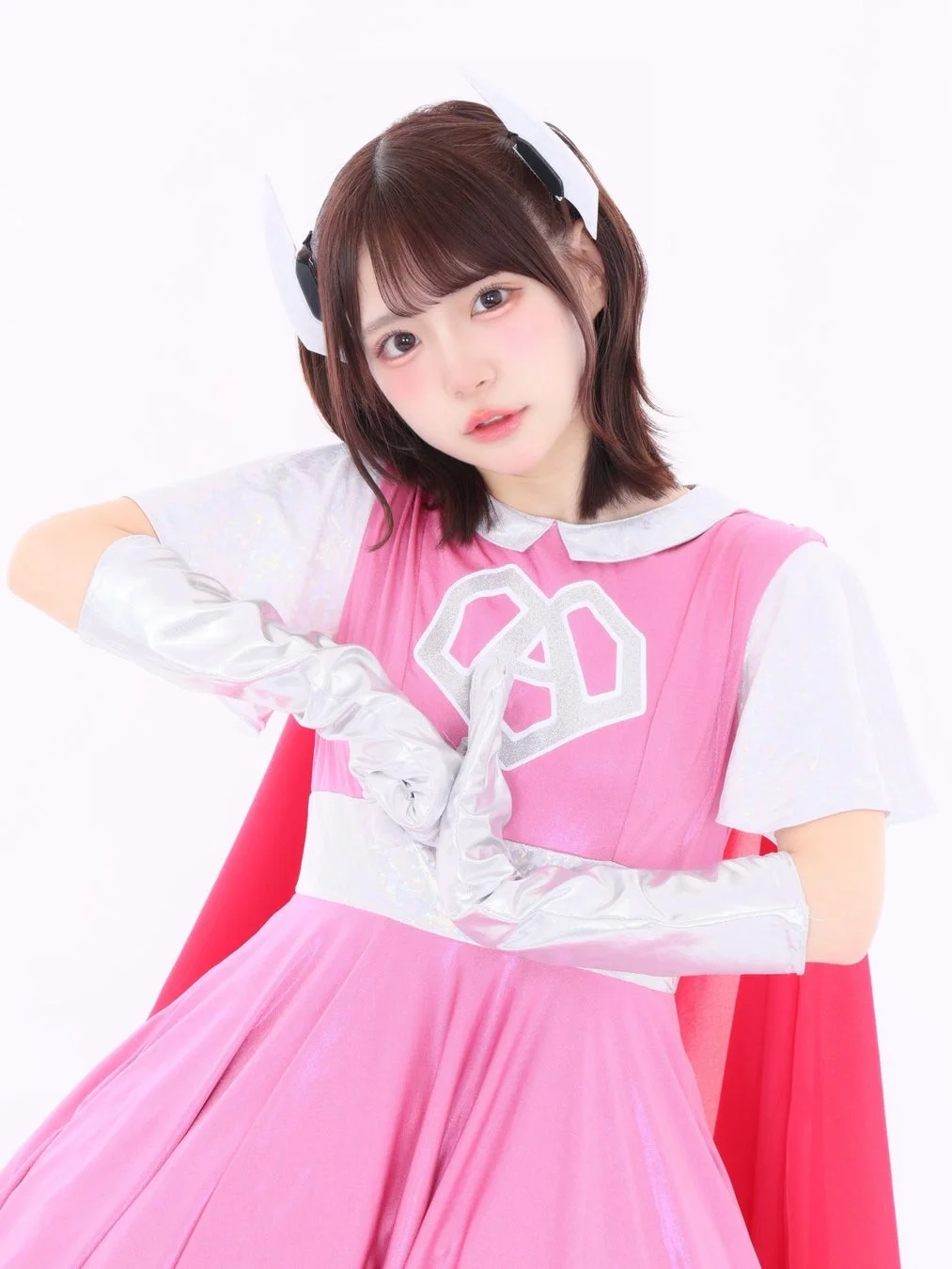 ピンクのドレスと赤いケープを身につけた女性アイドルがポーズ