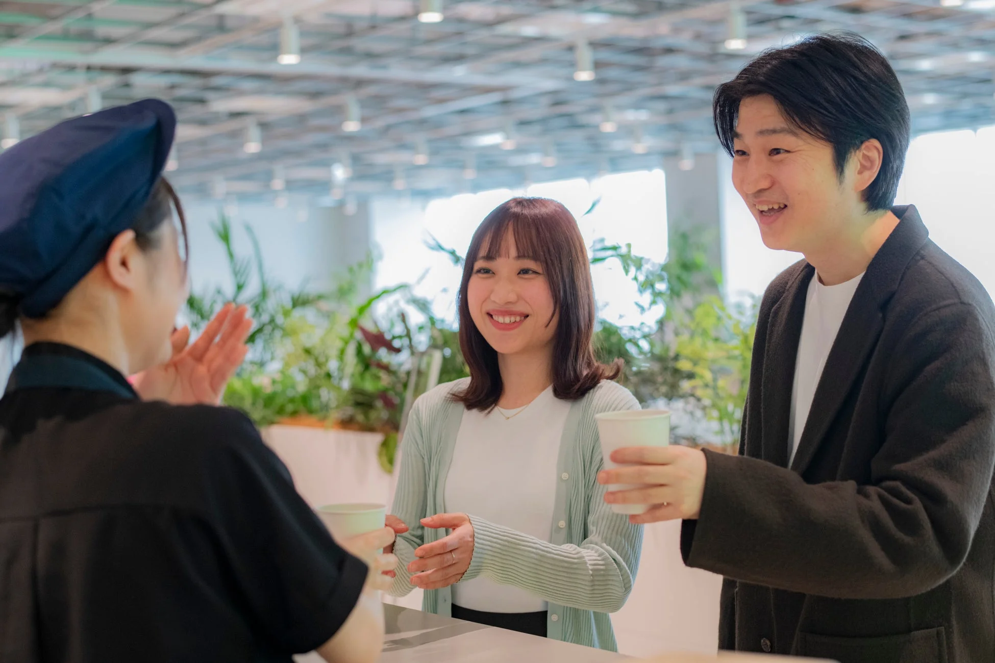 若い男女の客が笑顔でカフェの店員と会話しており、和やかな雰囲気