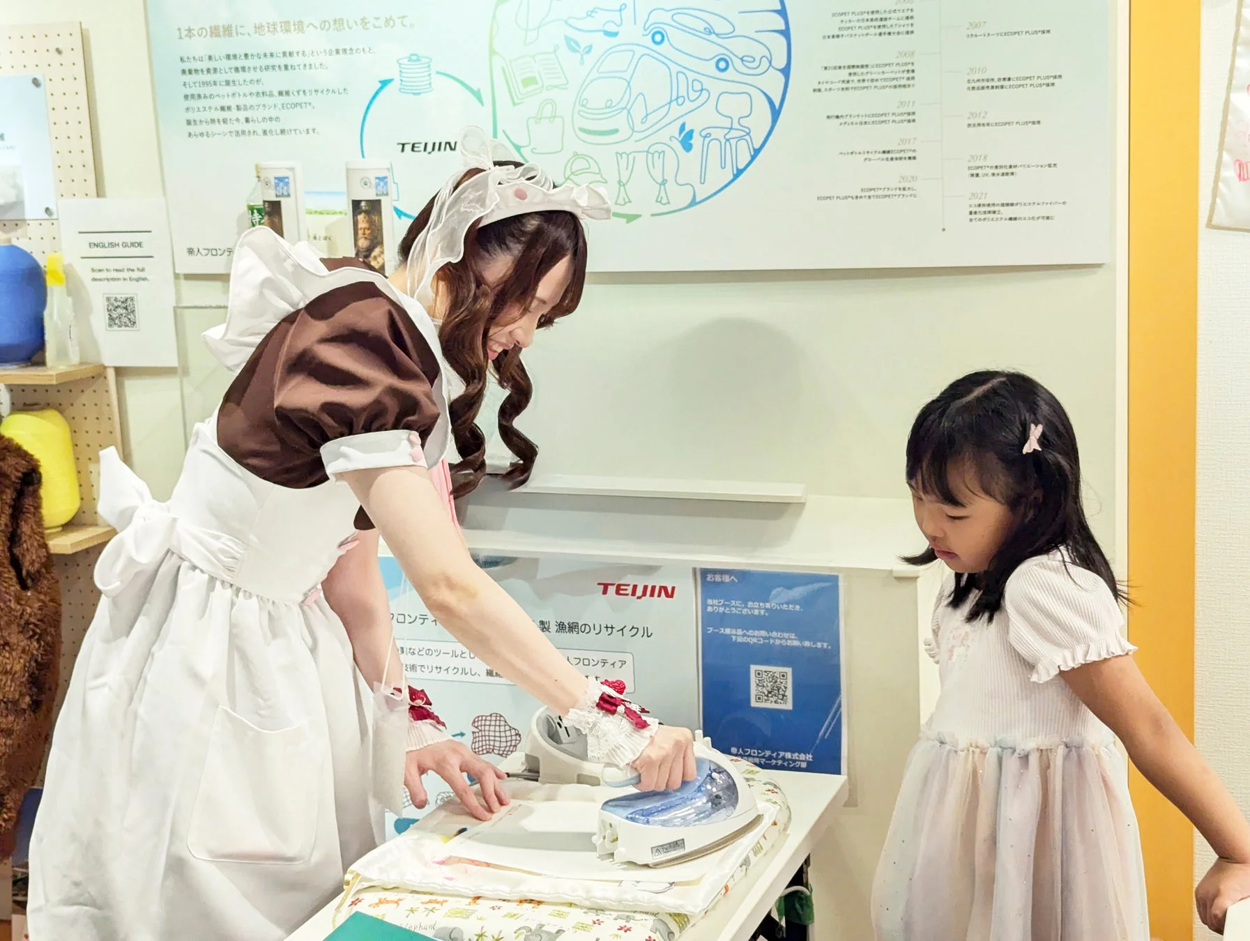 メイドさんが子どもにアイロンがけを実演している様子